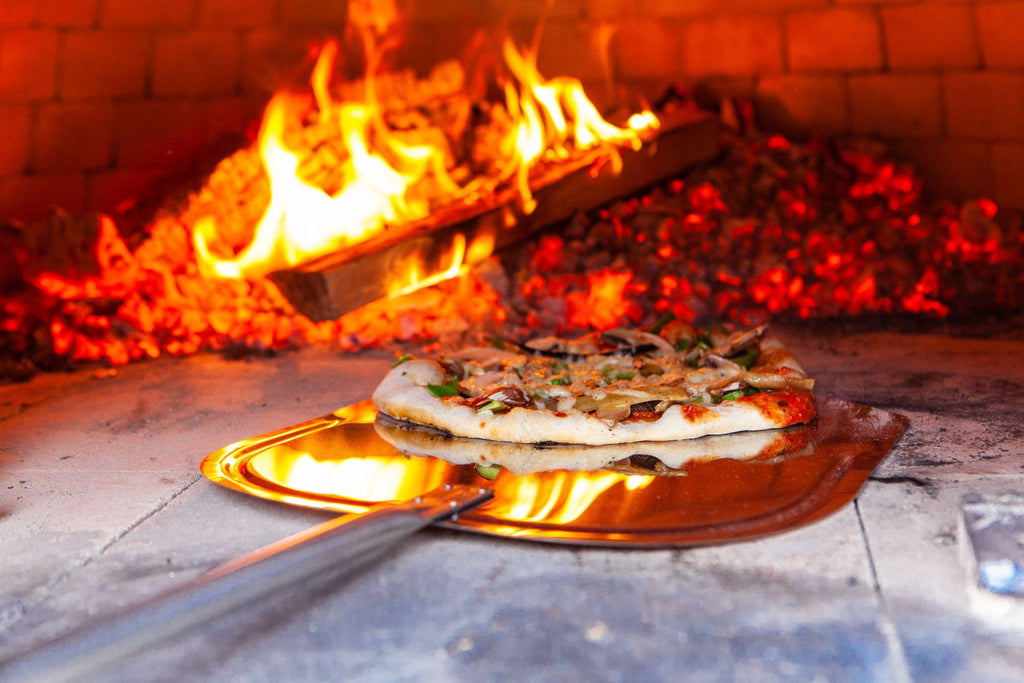 Man is placing a freshly prepared pizza into an outdoor bread oven